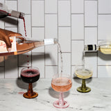 Wine being poured into glasses on a marble countertop with a tiled wall background