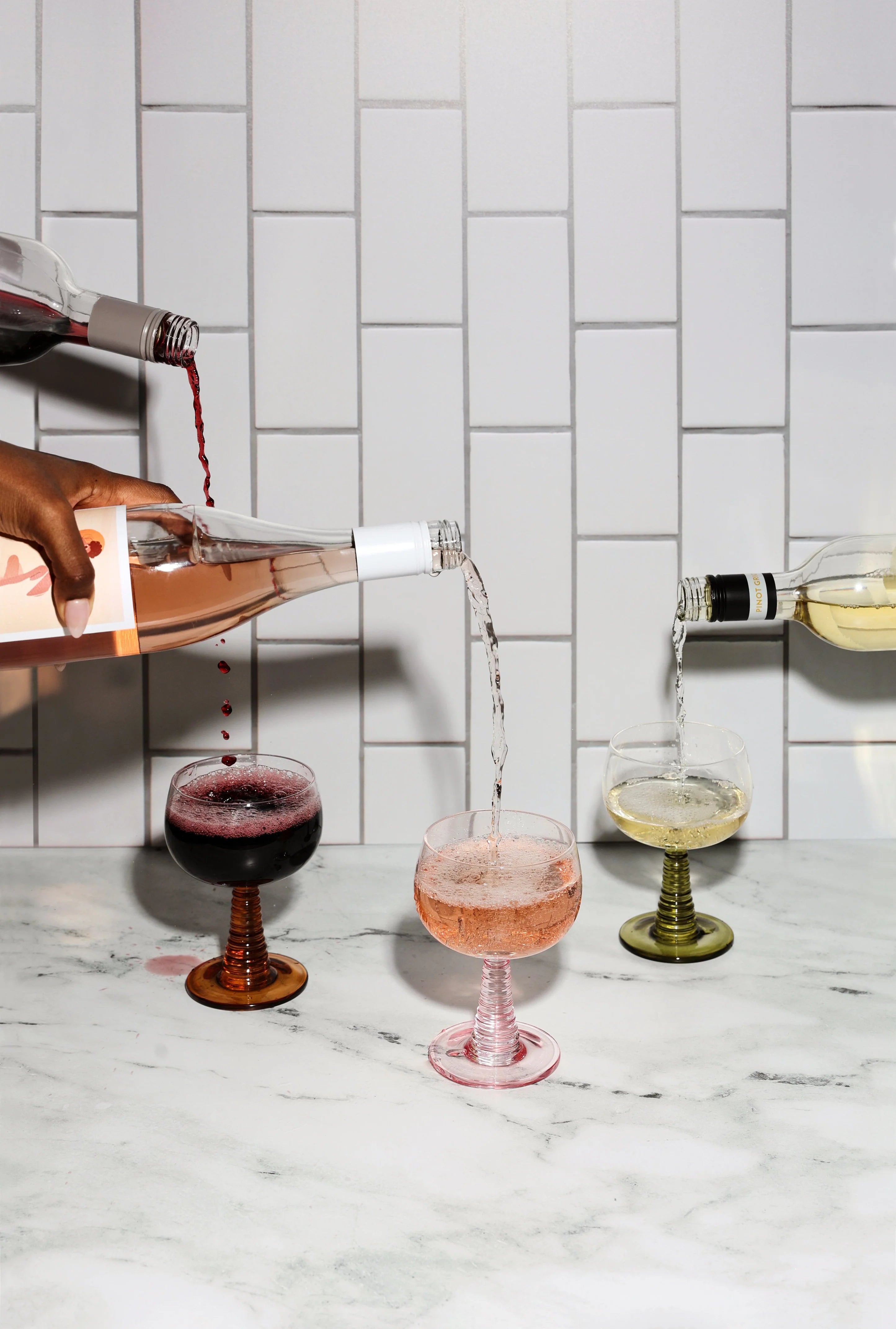 Wine being poured into glasses on a marble countertop with a tiled wall background